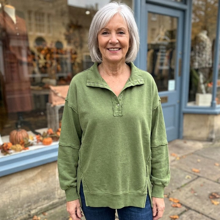 Hazel raw-edge henley sweatshirt in Olive, worn in front of a boutique