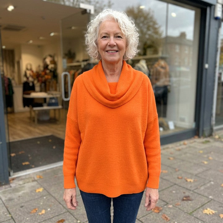 Juliette cowl neck jumper in Orange, worn in front of a boutique