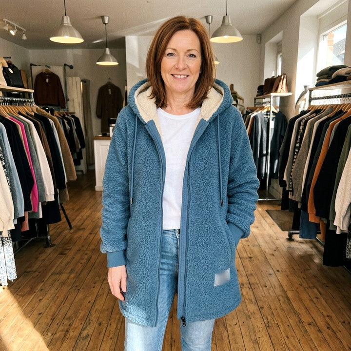 Phoebe cosy hooded jacket in Blue, worn in a boutique